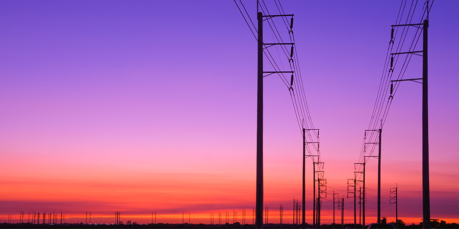 Electrical transmission lines stretching across the landscape during a vibrant sunset.
