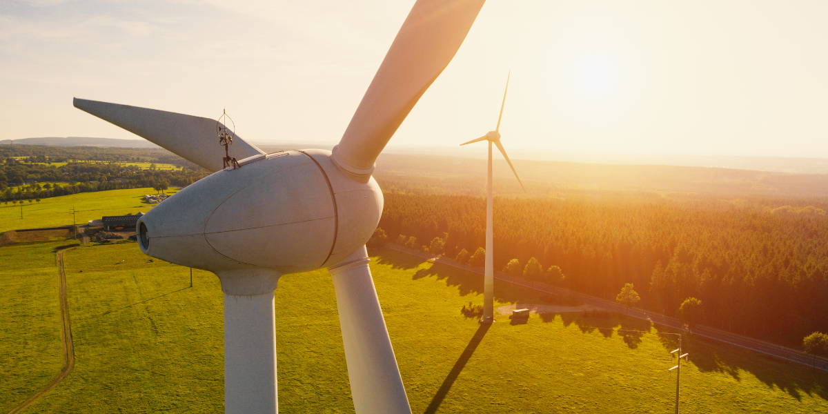 A technician working on a wind turbine at sunset with another turbine in the background, symbolizing renewable energy and sustainable power generation.