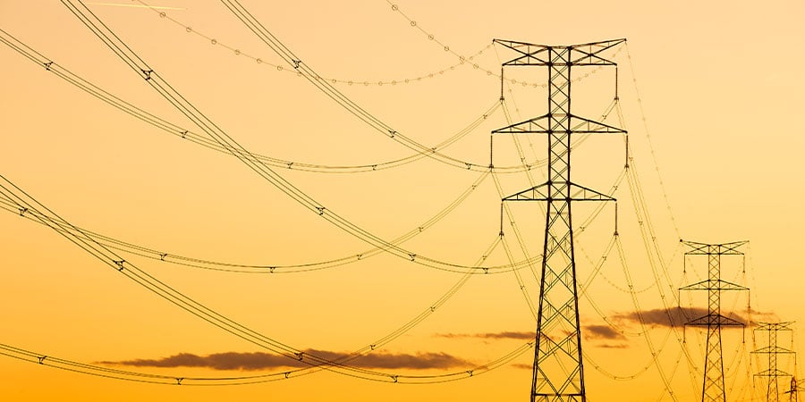 High-voltage power lines and steel lattice transmission towers silhouetted against a golden sunset sky.