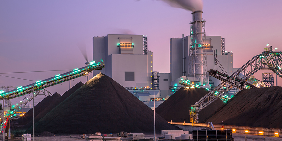 Coal-fired power plant with conveyors transporting coal piles at dusk.